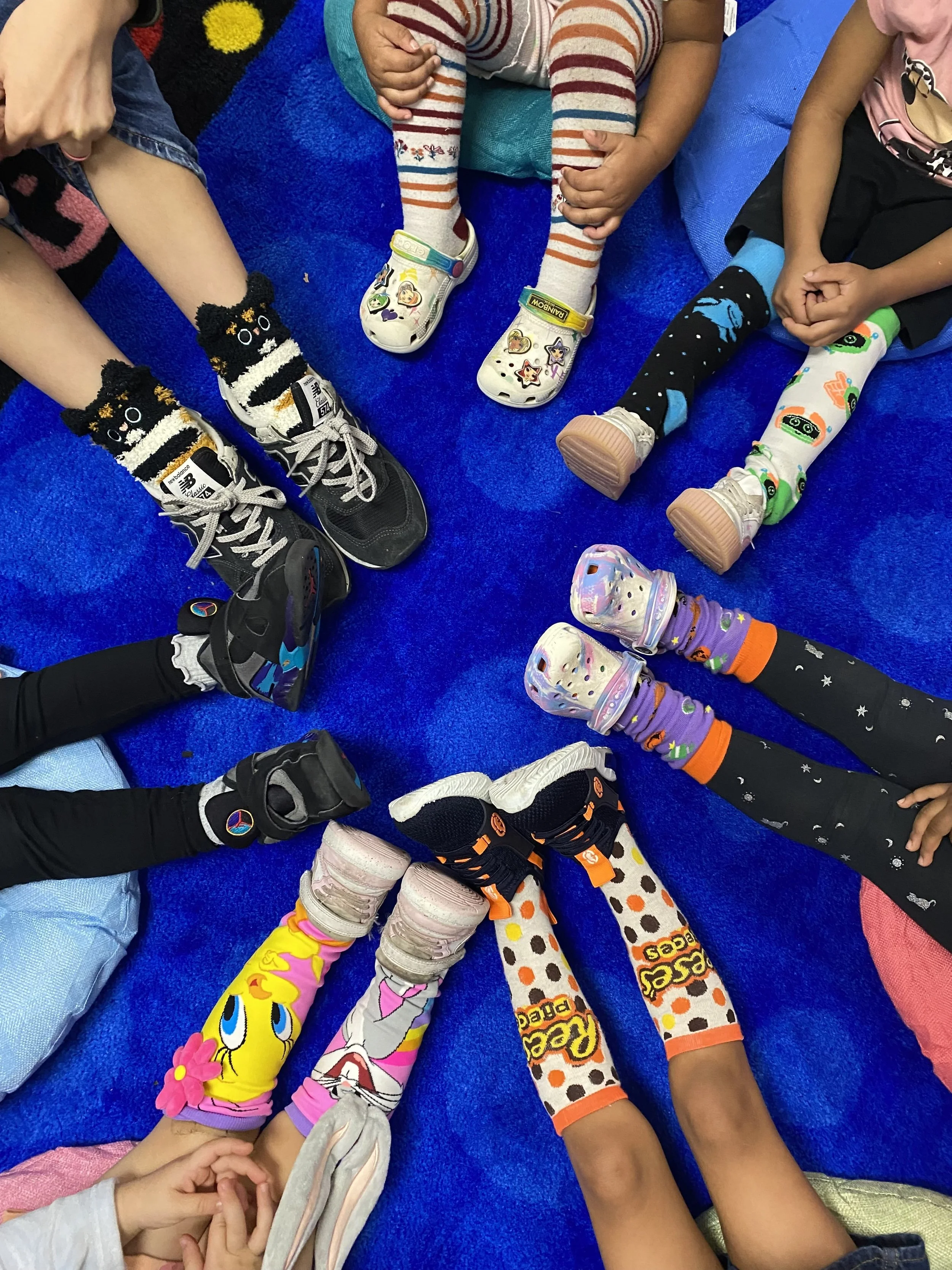 Circle time on the classroom rug with preschoolers sharing and comparing their colorful socks and shoes at Wesley Preschool in Austin, Texas