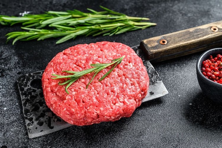 Raw ground beef patty with fresh rosemary on a butcher knife — ground beef makes up 40-50% of a beef share.