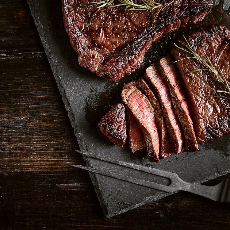 Sliced grilled steak on a slate board with rosemary — ranch-direct beef from Dry Creek Pastures.