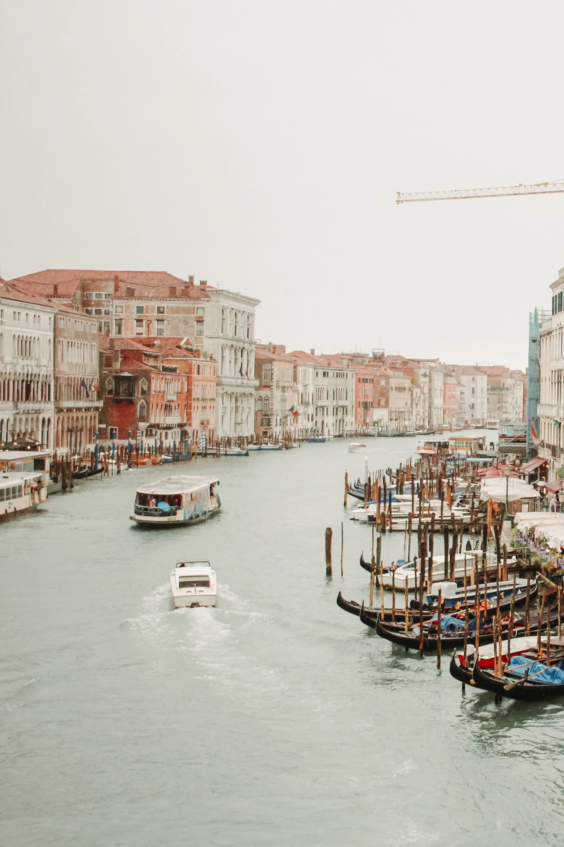 Photograph of Venetian canal with boats, gondolas, and historic buildings on either side under a cloudy sky.