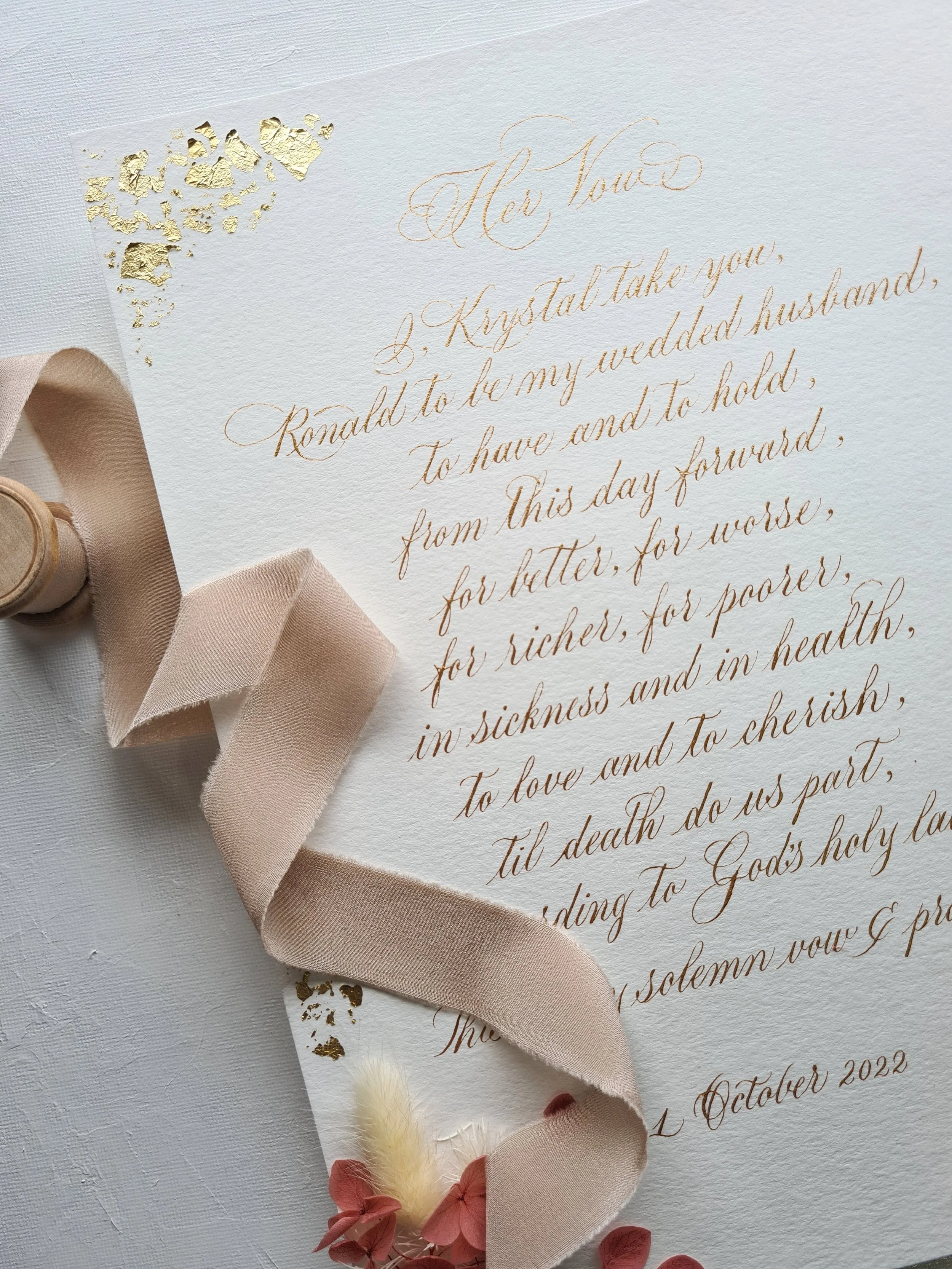 Wedding vow letter with gold leaf accents, beige ribbon, and decorative flowers.