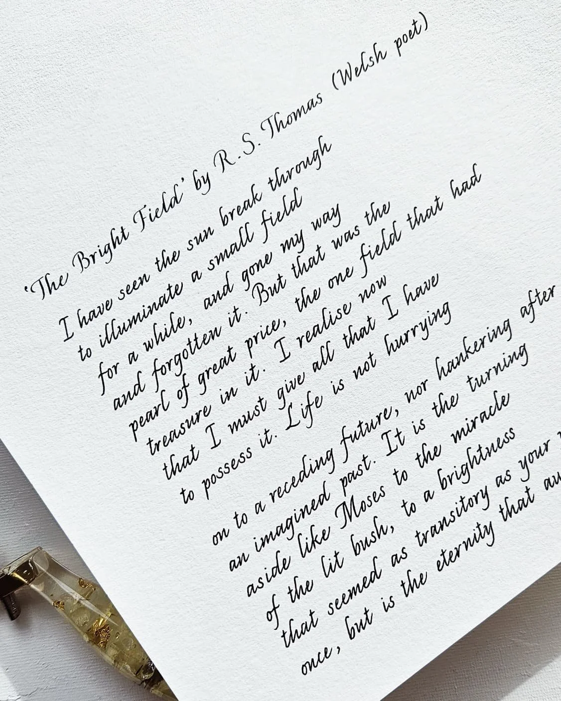A handwritten poem or quote on textured white paper, called "The Bright Field" by R. S. Thomas, Welsh poet, with a decorative pen in the bottom left corner.