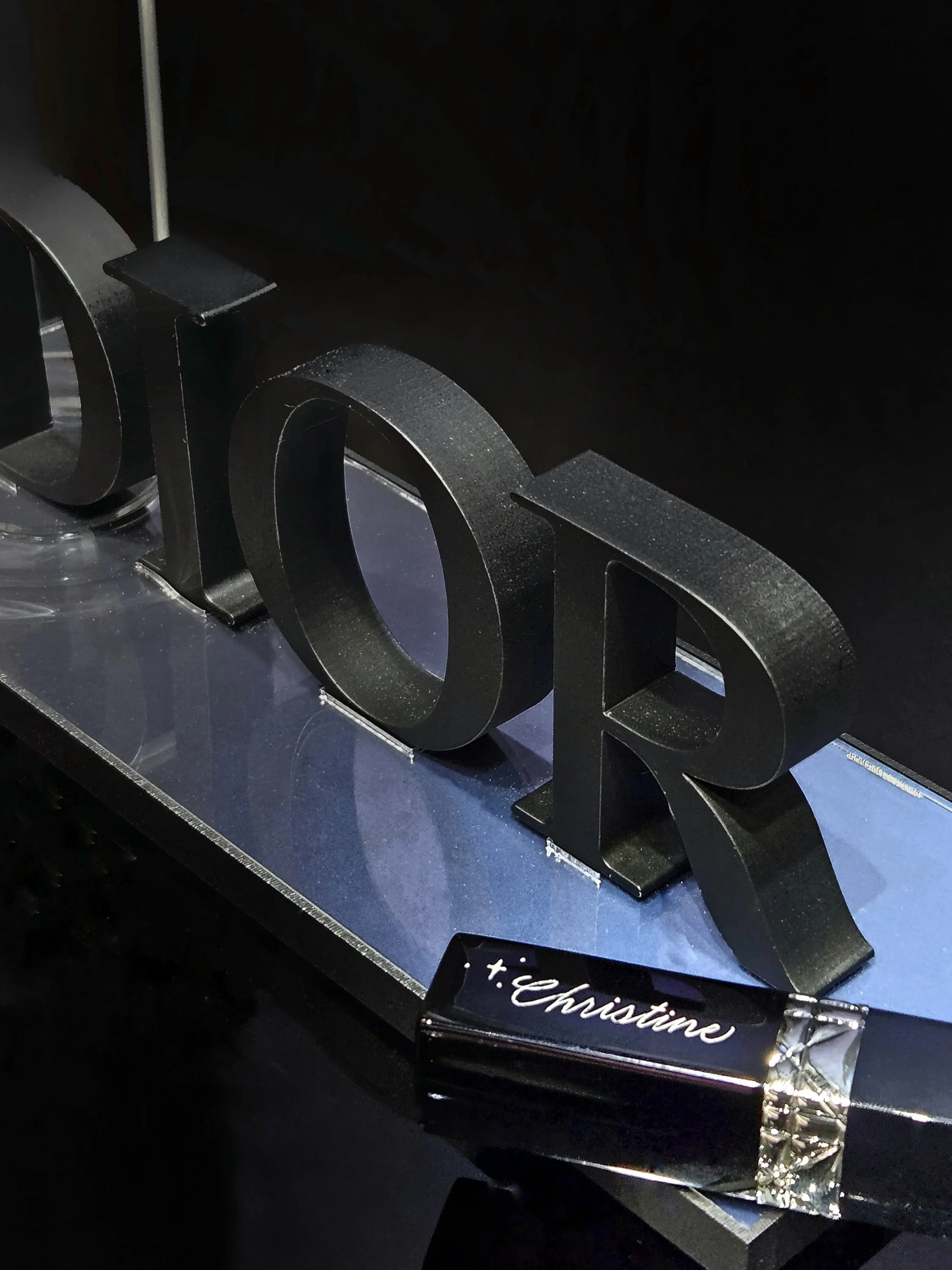 Black decorative letters spelling 'love' on a reflective surface, with a lipstick tube labeled '+.Christine' in the foreground.