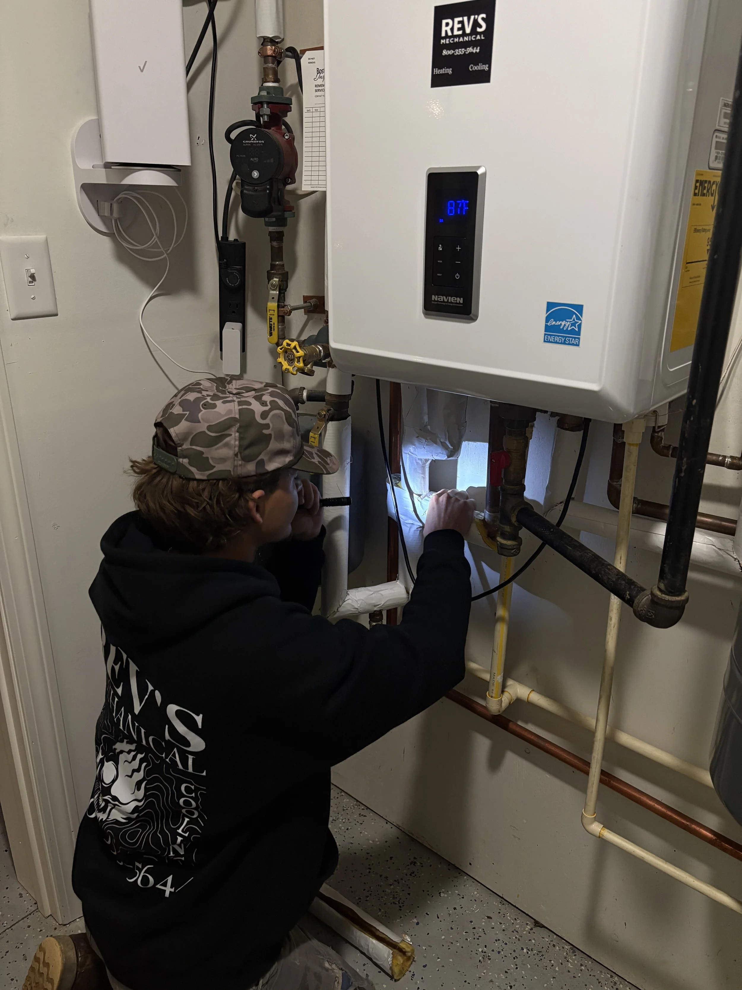 A person kneeling in front of a water heater, inspecting or repairing it, in a utility room.