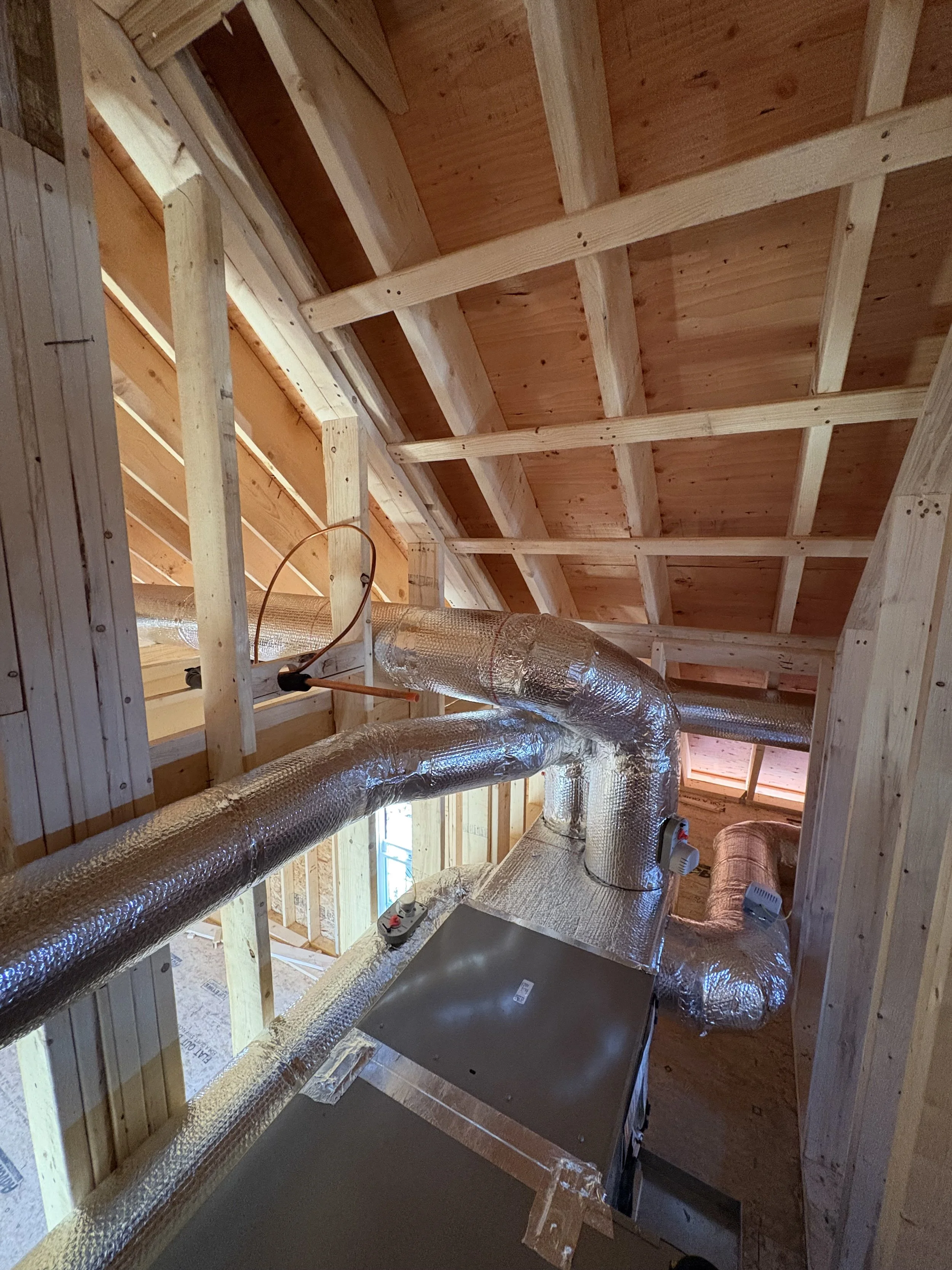 Insulation and ductwork installed in the attic of a wooden framed house under construction.