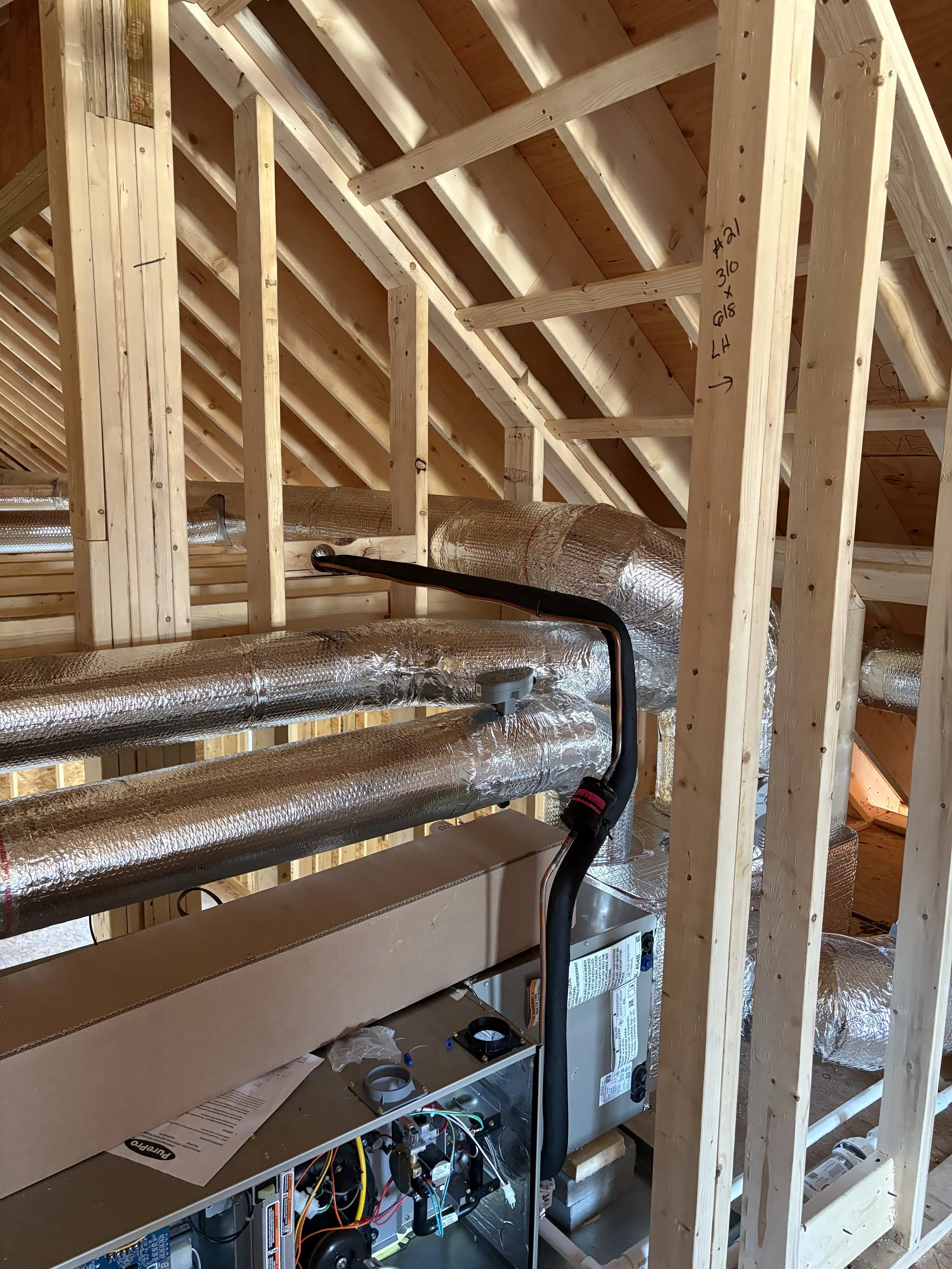 Construction of HVAC or ductwork system in an unfinished attic with wooden framing, insulated ducts, and heating or cooling units.