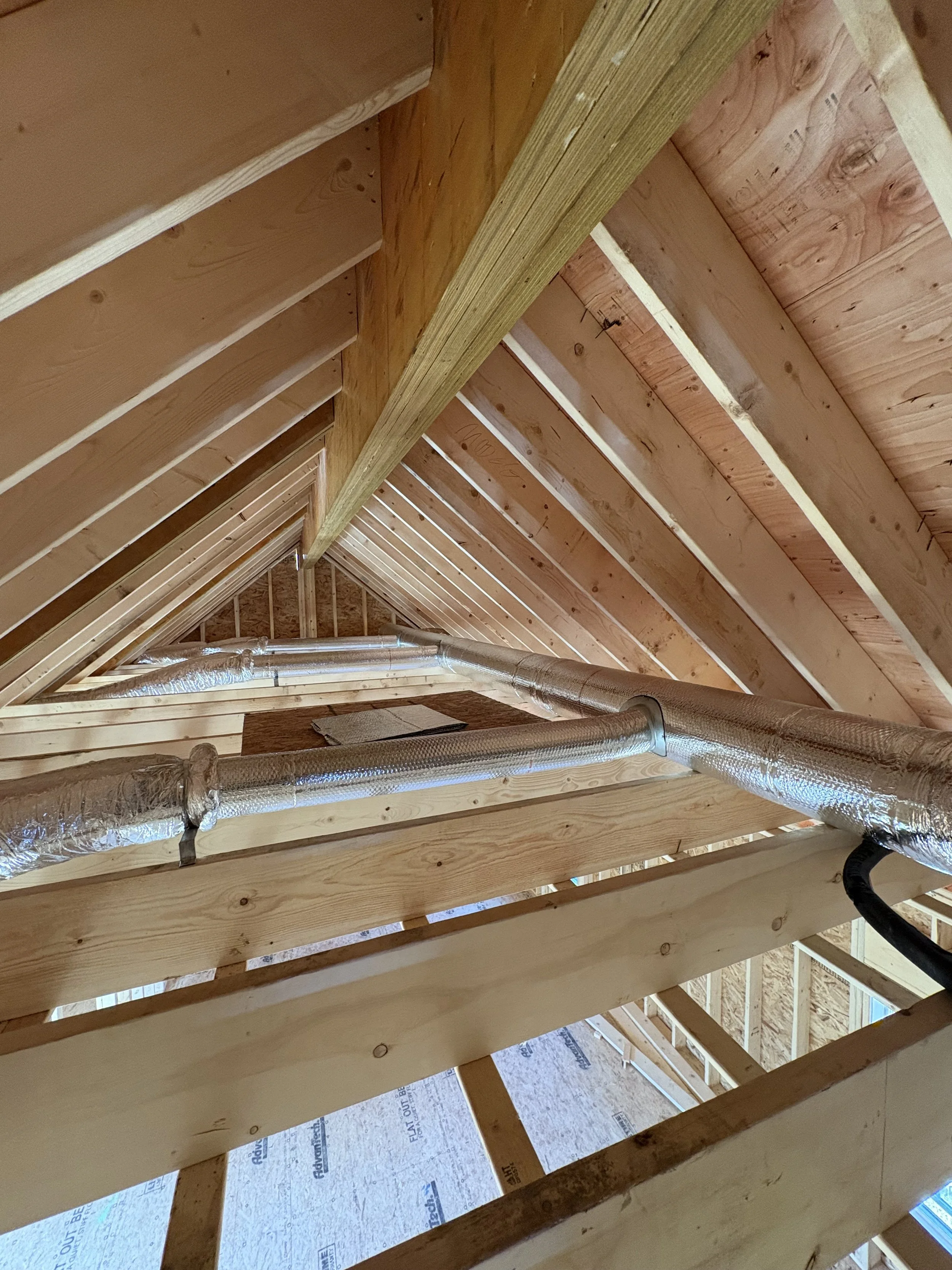 View of an unfinished attic with wooden framing and silver insulated ductwork.