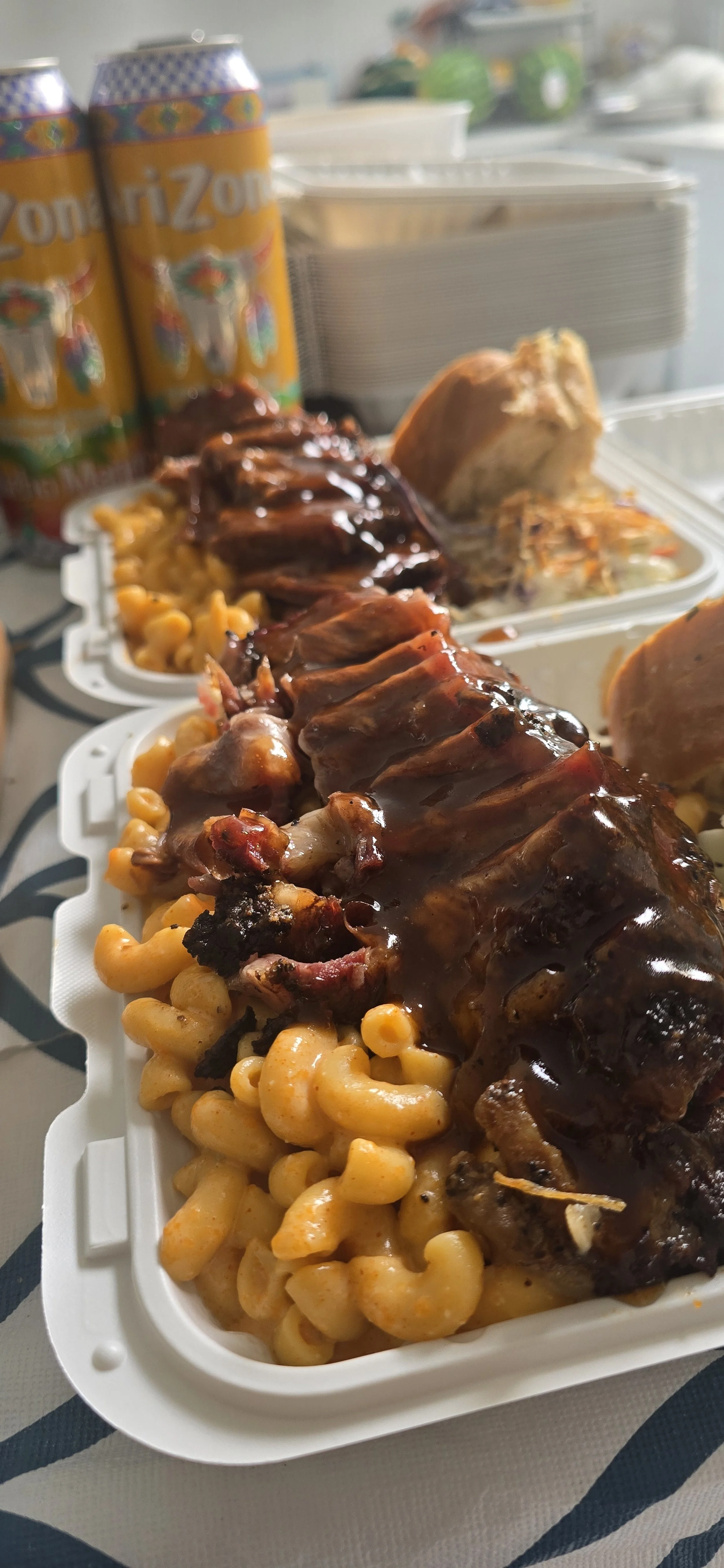 Barbecue ribs with macaroni and cheese, garlic bread, and coleslaw in a to-go container, with soda.