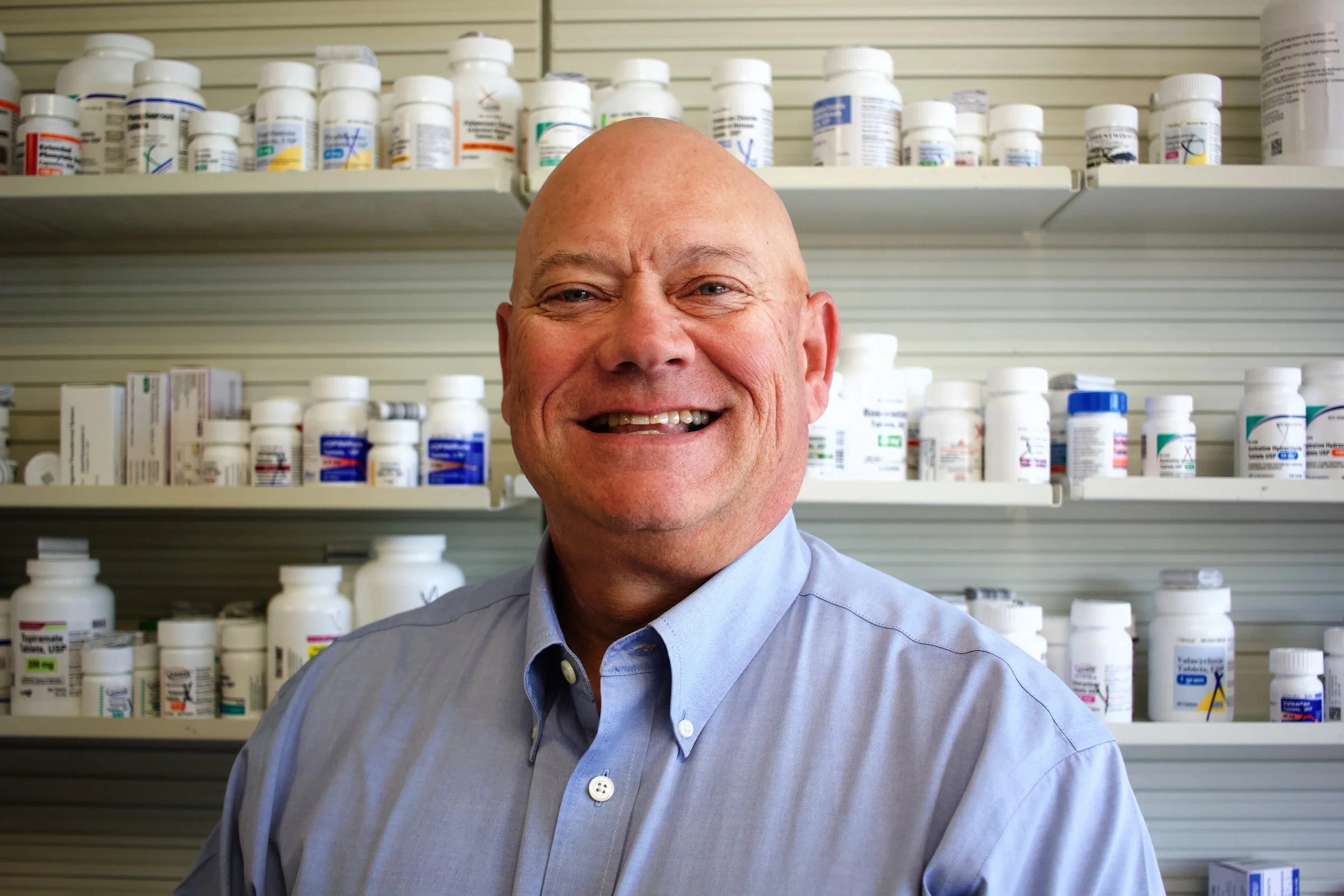 A pair of hands measuring a light brown dog with a tape measure, outdoors, with a grassy field and dirt path in the background.