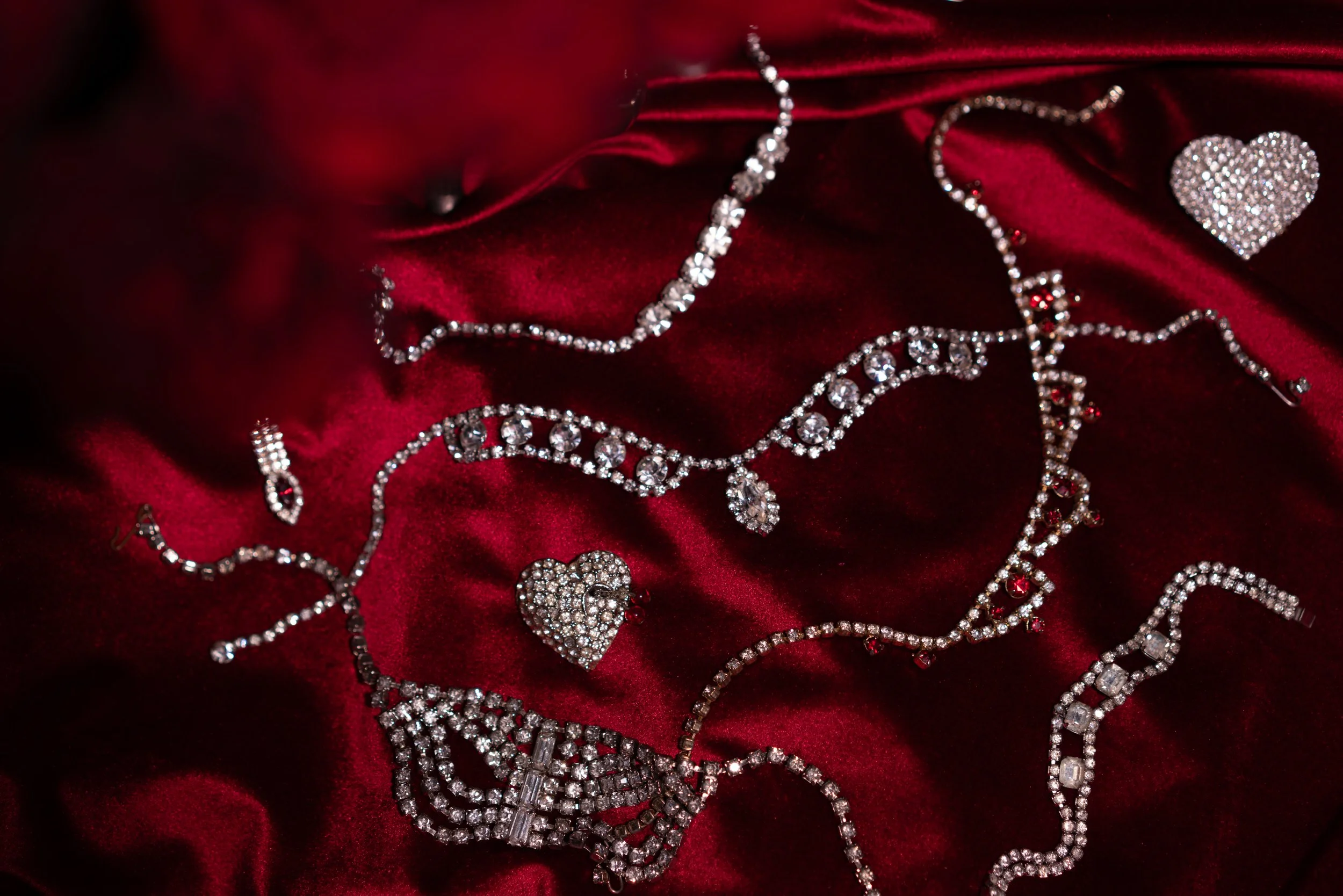 Various sparkling jewelry pieces, including necklaces, earrings, and a heart-shaped pendant, arranged on red satin fabric.