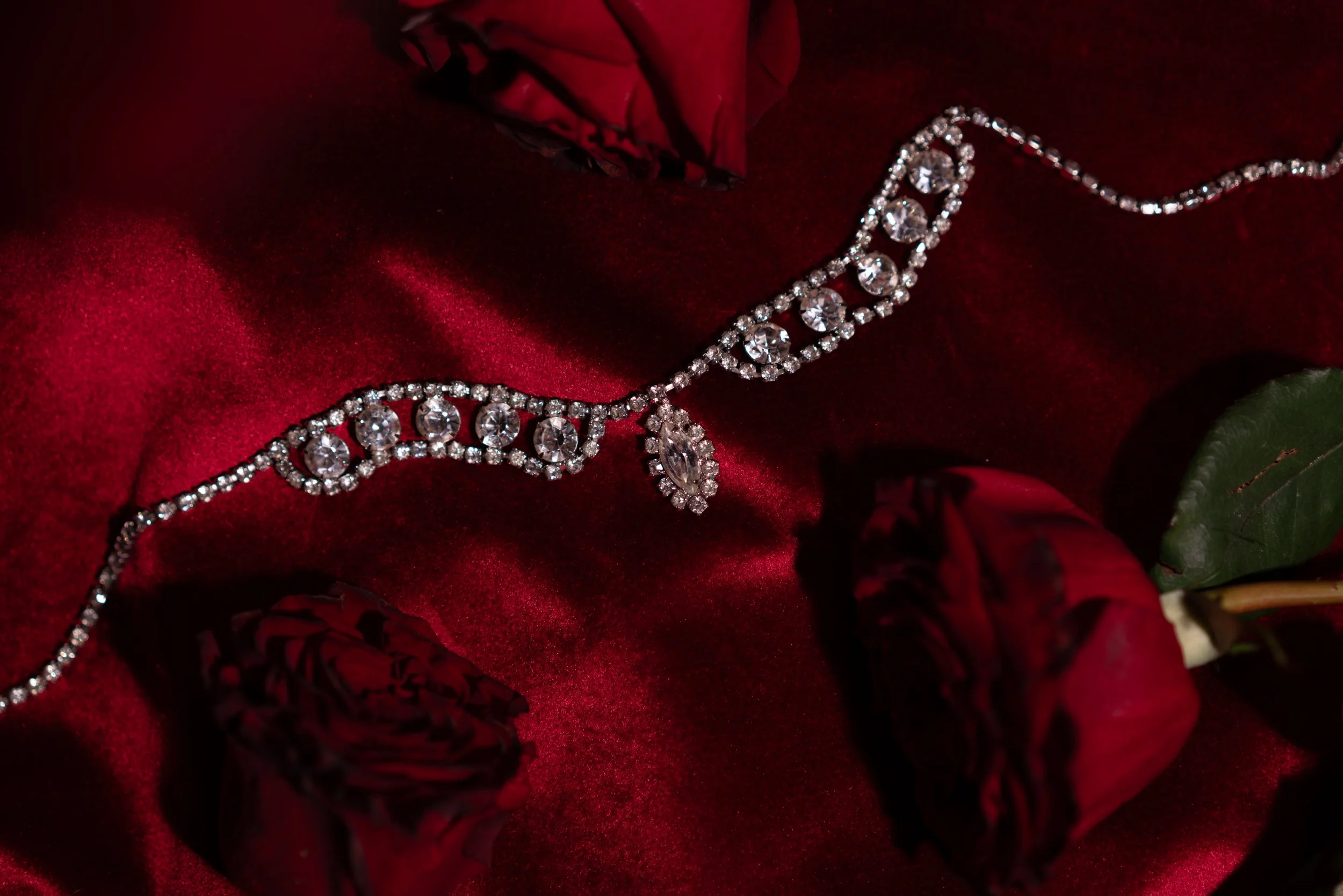 A diamond necklace resting on red satin fabric with red and black roses nearby.