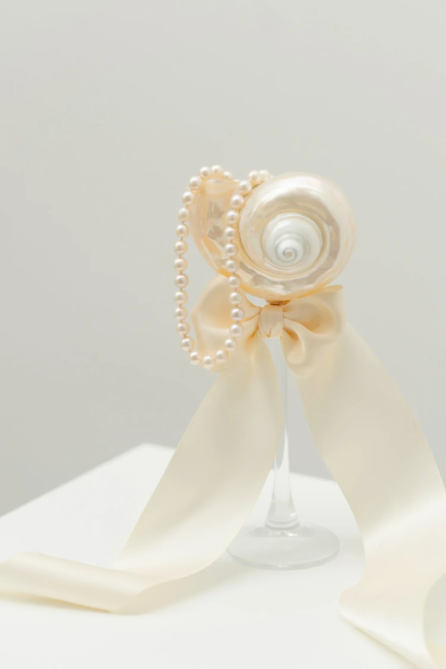 Decorative seashell with pearl necklace, satin ribbon bow, and long satin ribbon on display.
