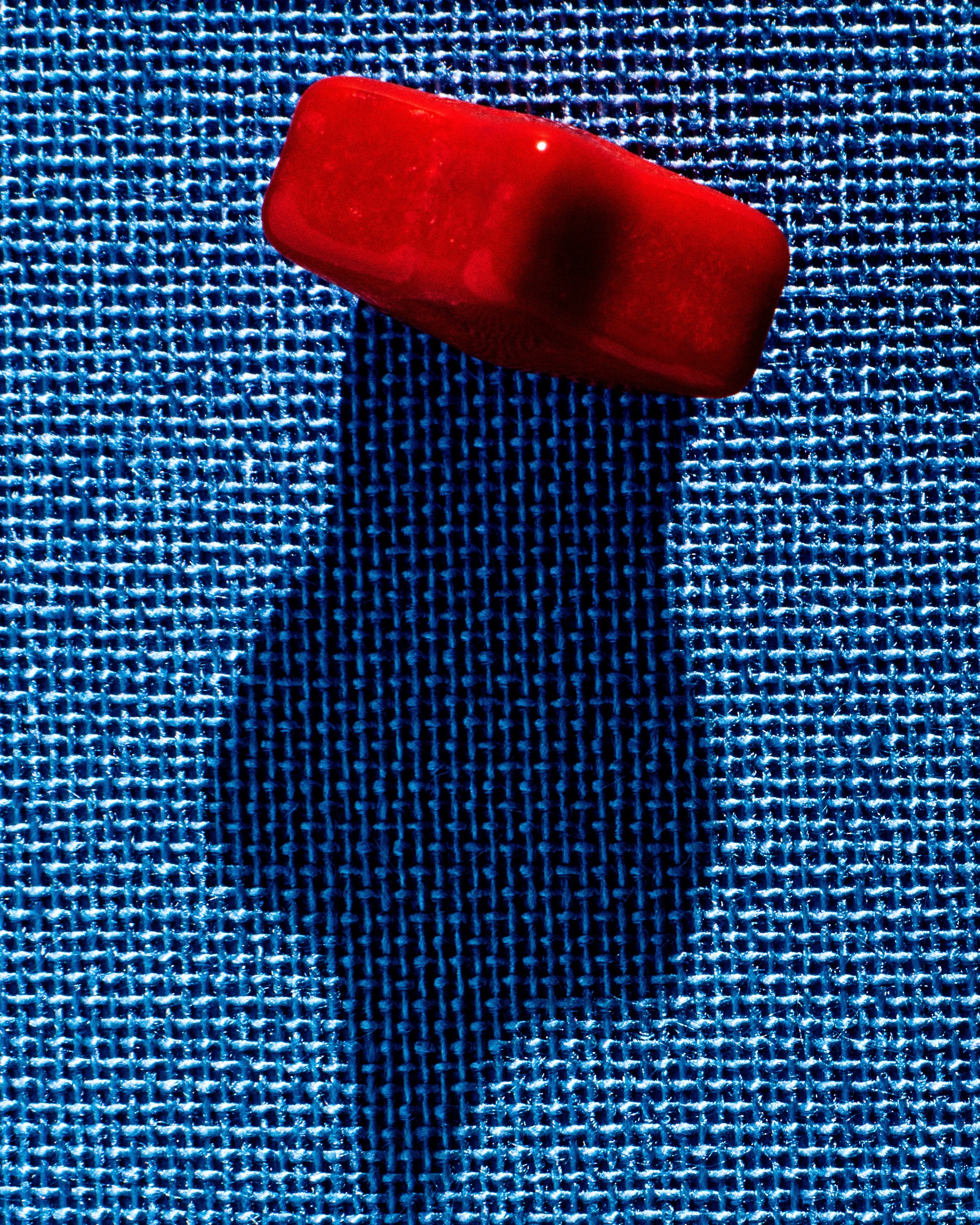 A single red pill resting on a textured blue fabric surface.