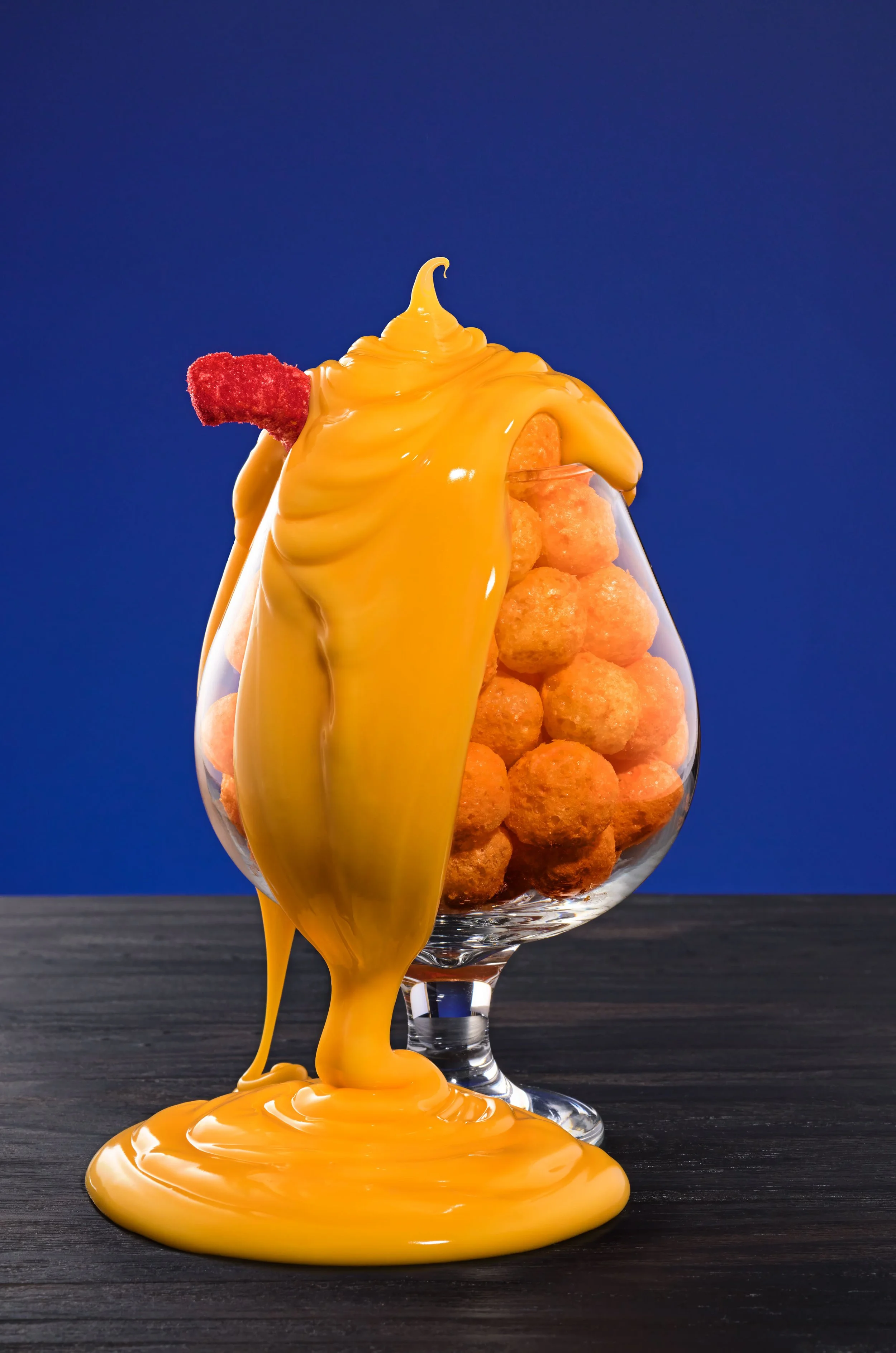 A glass filled with cheese balls, with melted cheese spilling over the top and cascading down the side.