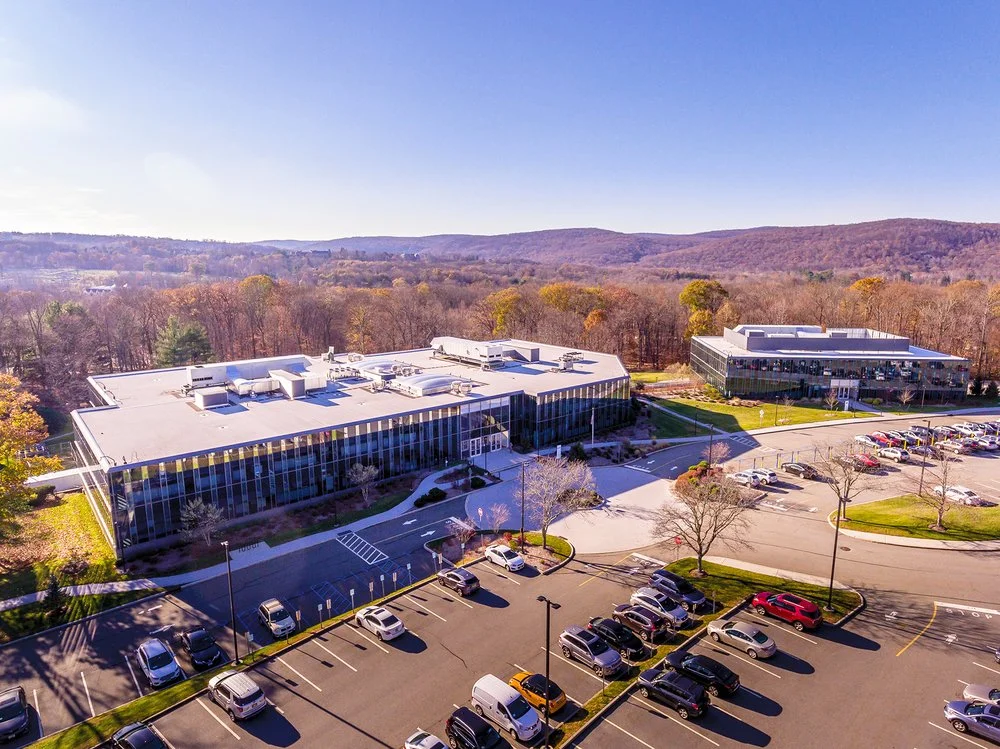 Aerial view of a modern office building complex in Mahwah, New Jersey with a parking lot in the foreground, surrounded by trees and hills under a clear blue sky. JordyClean provides Commercial cleaning service in Mahwah, NJ.