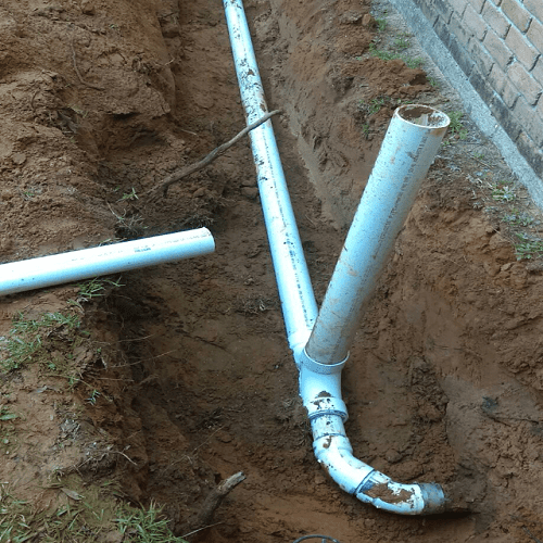 Underground drainage pipes installed in a trench next to a brick wall.