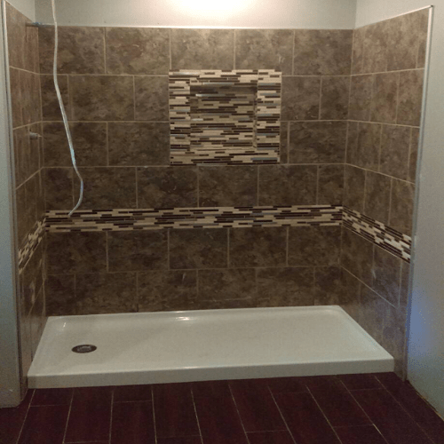 Empty shower with brown tiled walls and a decorative mosaic strip, a built-in niche, and a white shower pan.