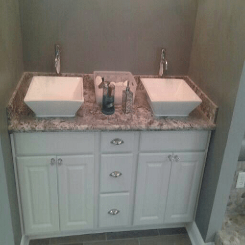 Bathroom vanity with double sinks, granite countertop, white cabinets, and dual faucets
