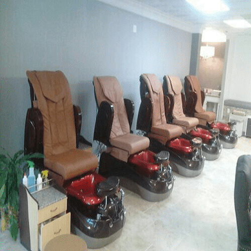 Five pedicure chairs with foot baths in a salon, arranged in a row against a wall.
