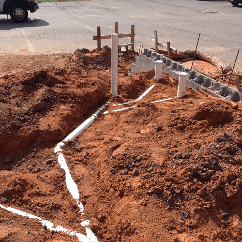 Construction site with existing underground plumbing pipes and partially built cinder block wall.