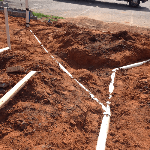 Excavated dirt with white PVC pipes laid in the trench for plumbing installation.