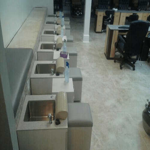 Row of handwashing sinks with soap dispensers and paper towel holders in a room with tiled floor and office desks in the background.