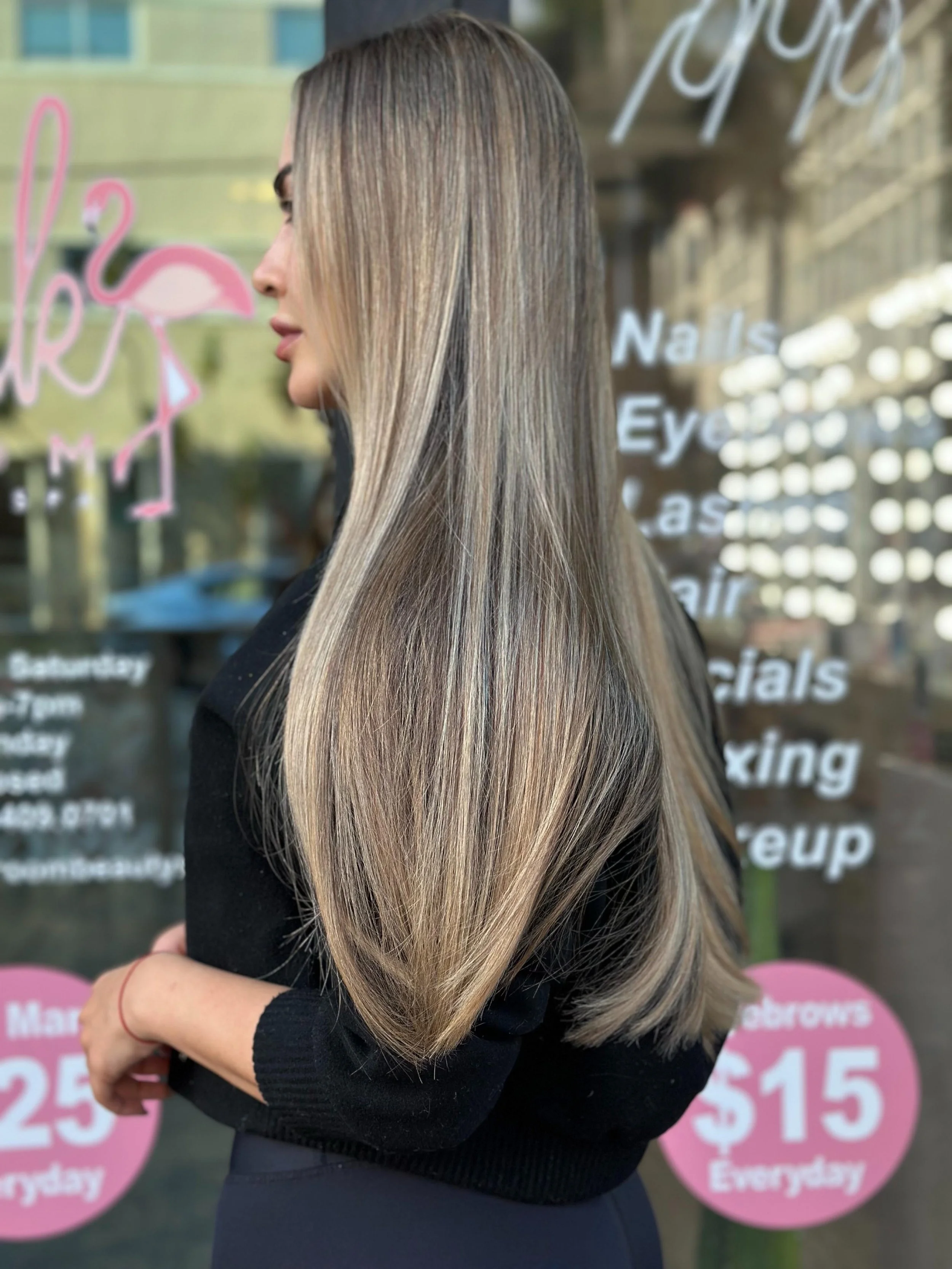 A woman with long, straight, blonde hair standing outside a beauty salon window.