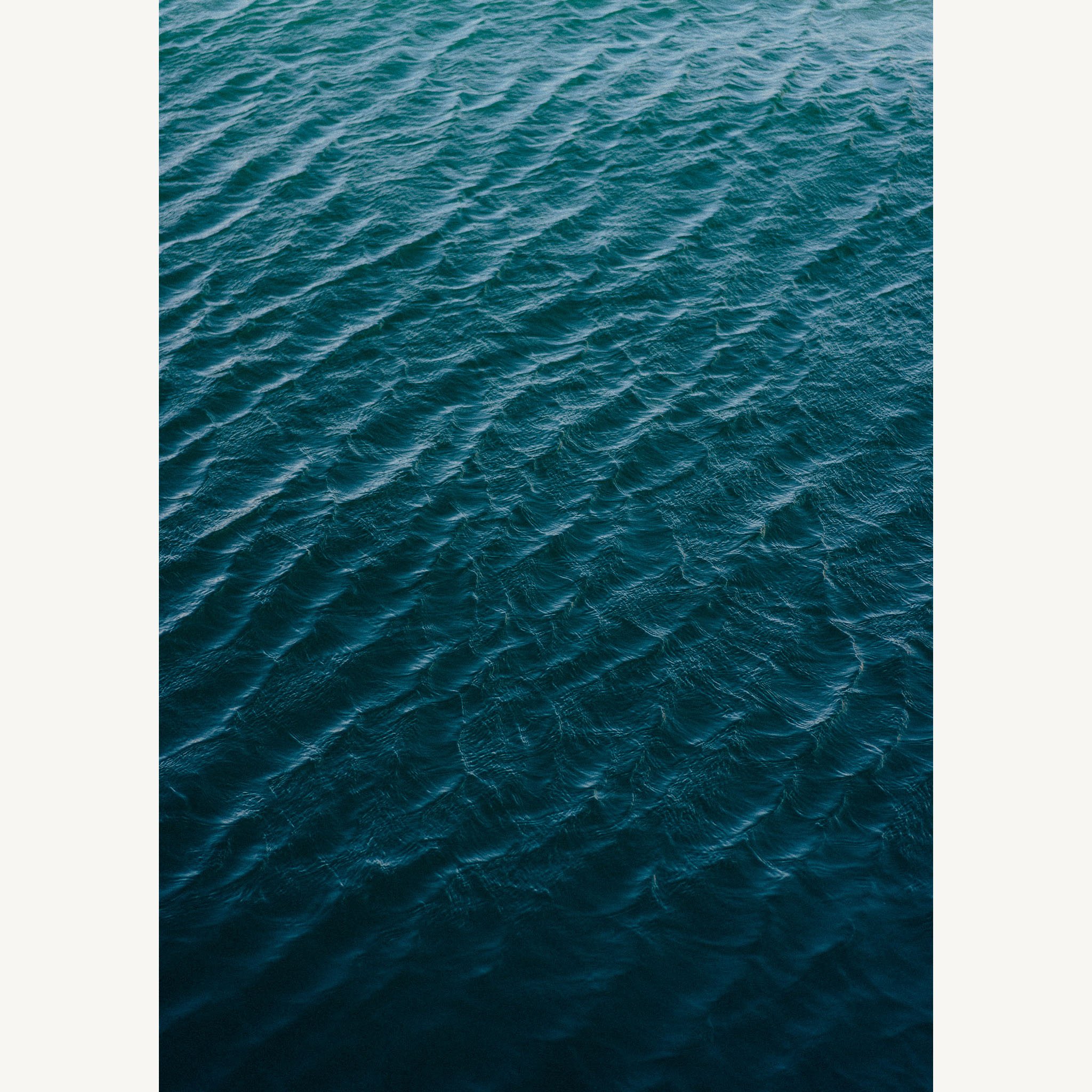 Abstract aerial photograph of deep blue ocean water, with shifting light and gentle movement creating subtle patterns across the surface.