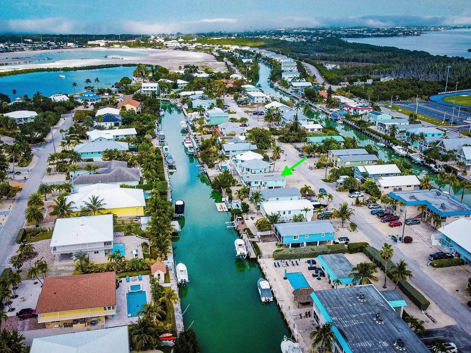 Aerial view of a coastal neighborhood with colorful houses along a canal with boats, palm trees, and a lake in the background.