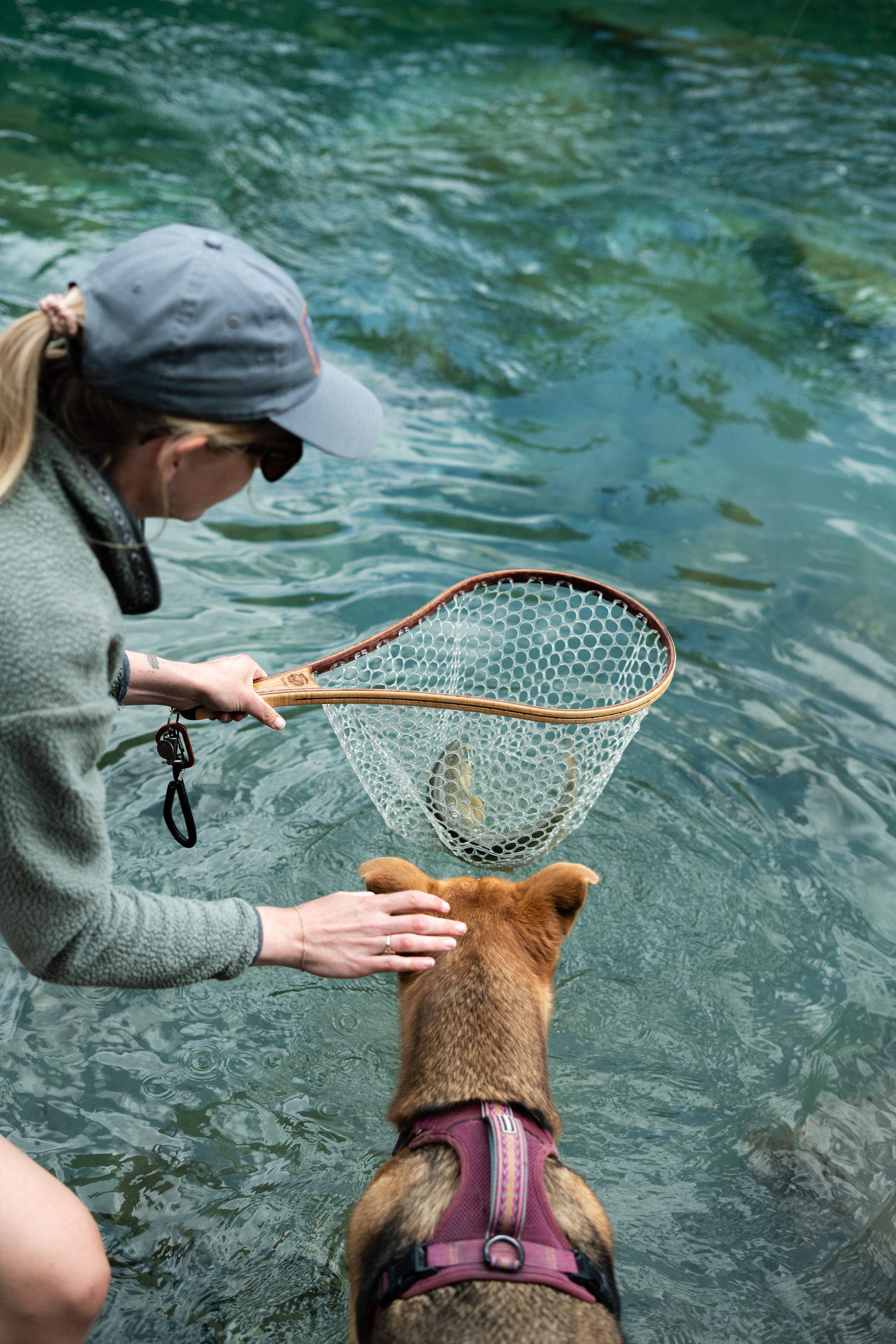 A girl with a cutthroat trout in a net, with a brown dog looking into the net
