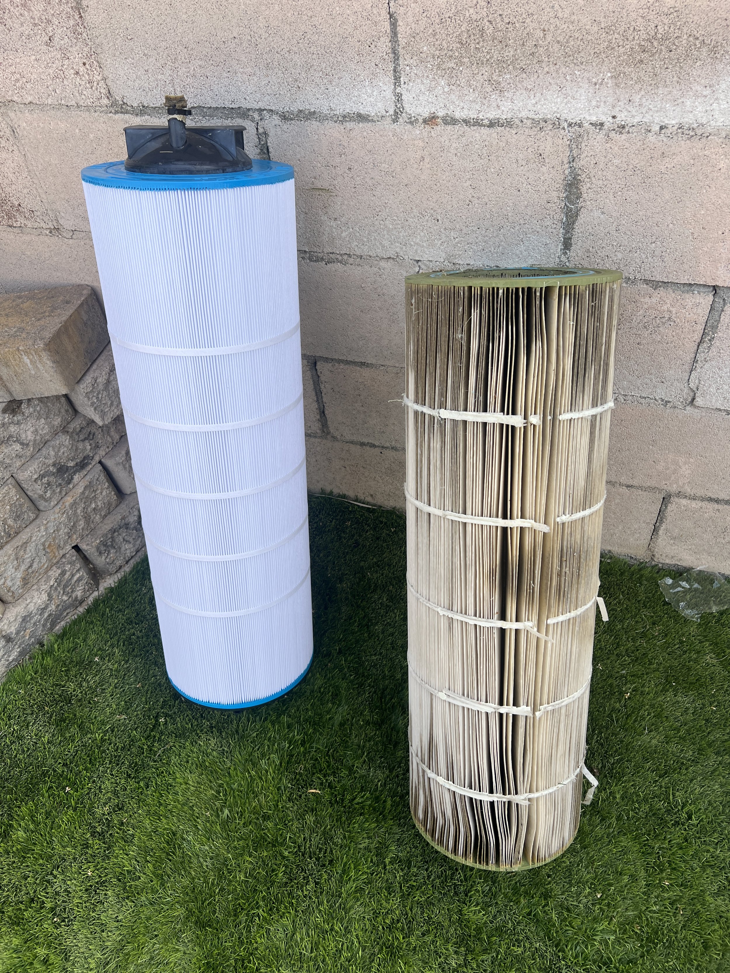 A brand New Clean Pool Filter Laying next to an old dirty Pool Filter on a patch of grass.