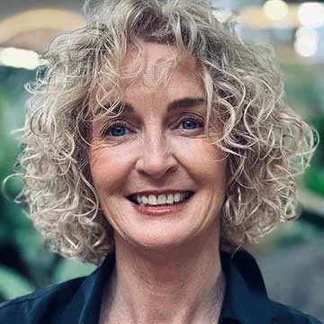 Close-up of a woman with curly blonde hair smiling, outdoors.