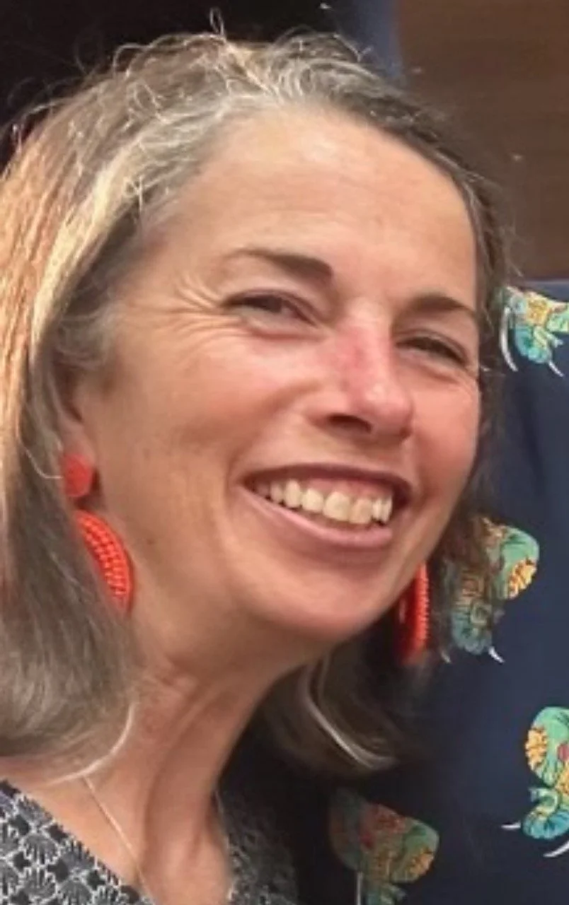 Close-up of a woman with gray hair smiling and wearing orange earrings.
