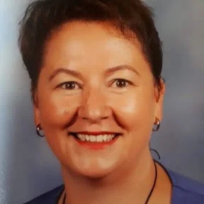 Close-up of a woman with short brown hair, smiling, against a light blue background.