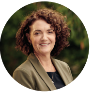 A woman with curly brown hair smiling outdoors, wearing a green jacket.