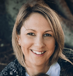 A woman with shoulder-length light brown hair, smiling outdoors with a blurred natural background.