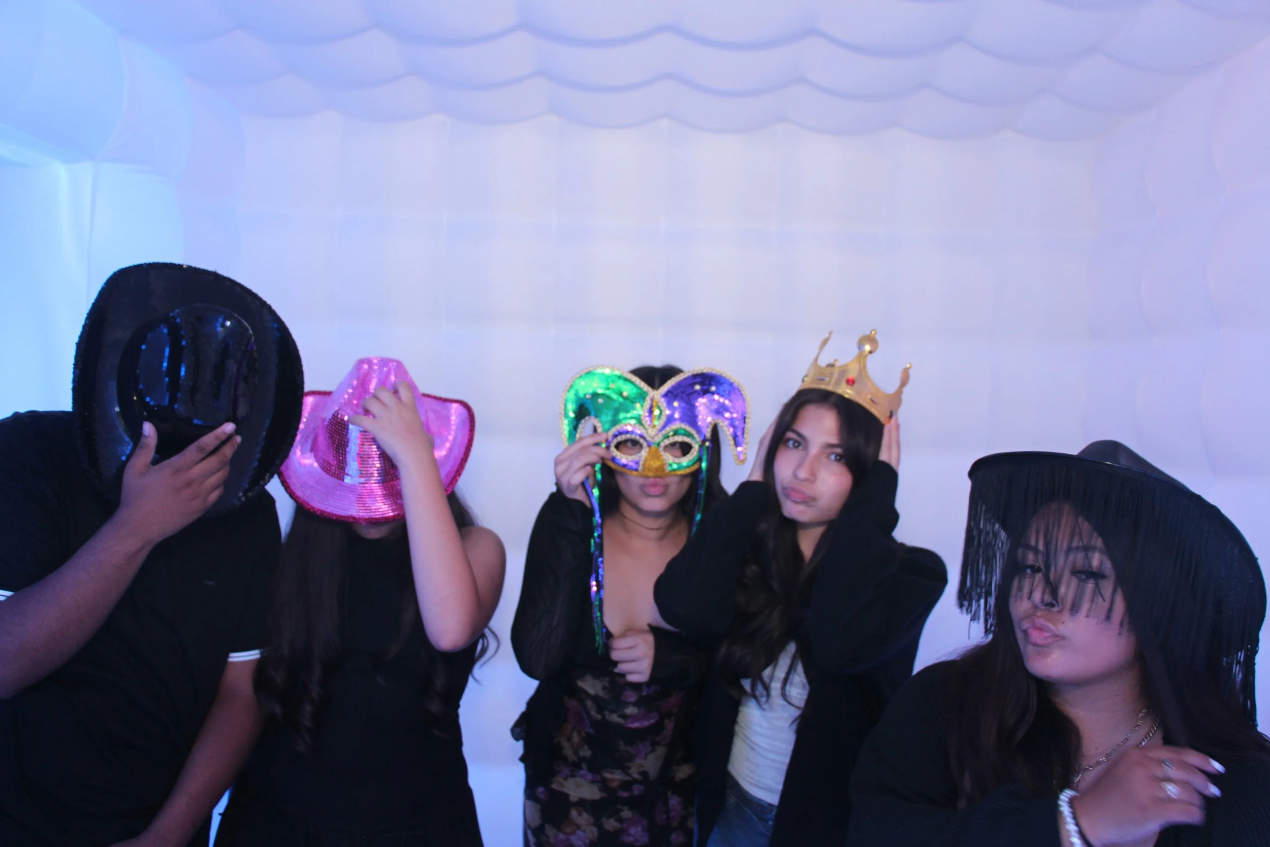 Group of five people at a party wearing colorful masks and hats, some making playful facial expressions.