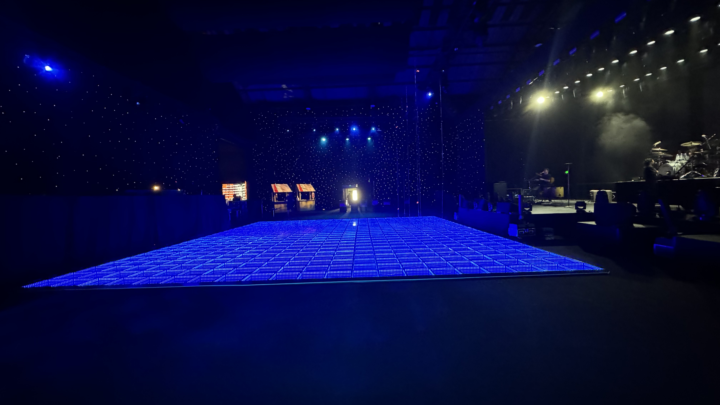 Empty stage with blue illuminated dance floor and band setup, in a dark venue with starry light effects on the walls.