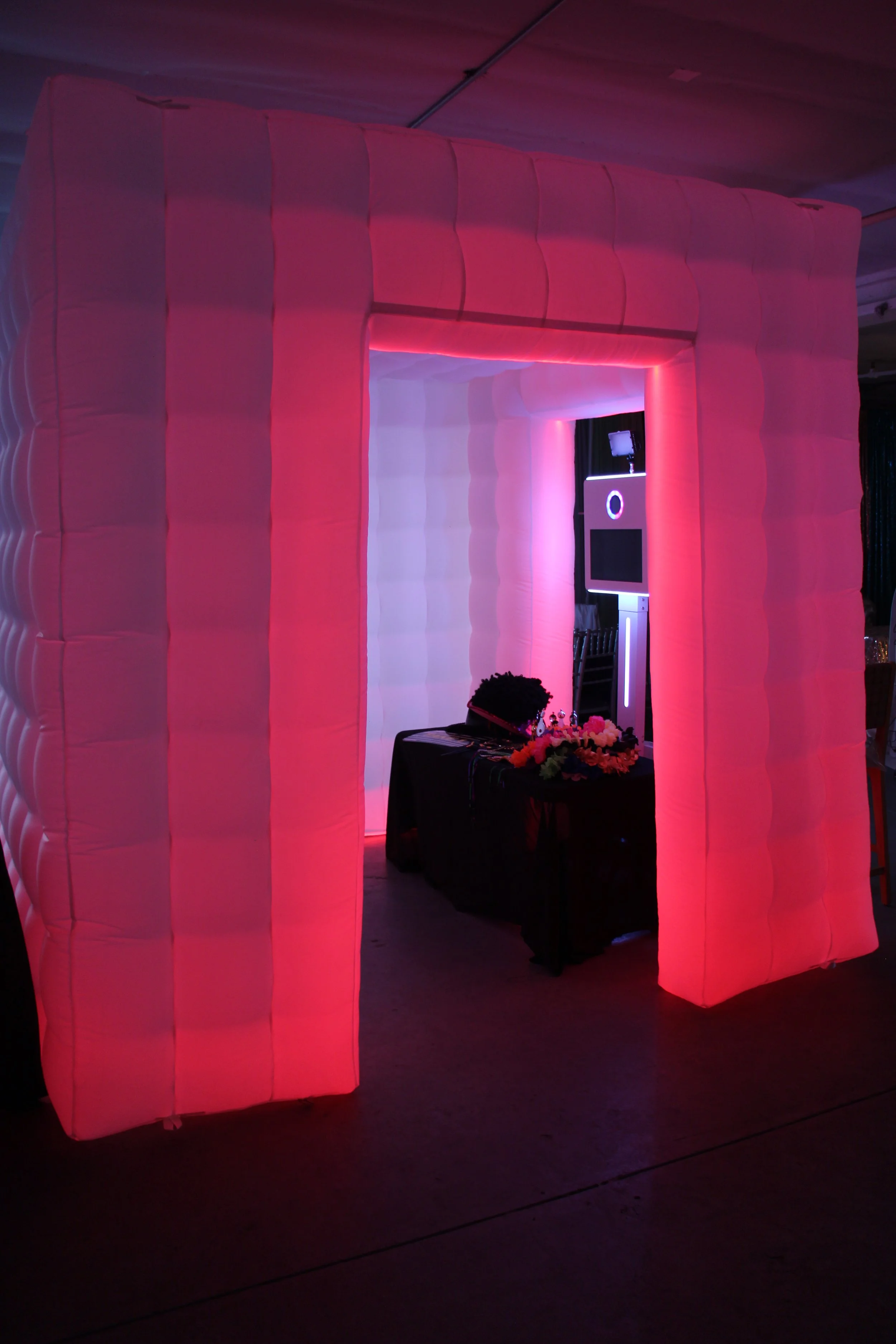 Colorful photo booth with illuminated pink and white padded walls and a screen inside.