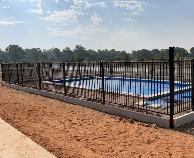 An outdoor swimming pool surrounded by a black metal pool fence