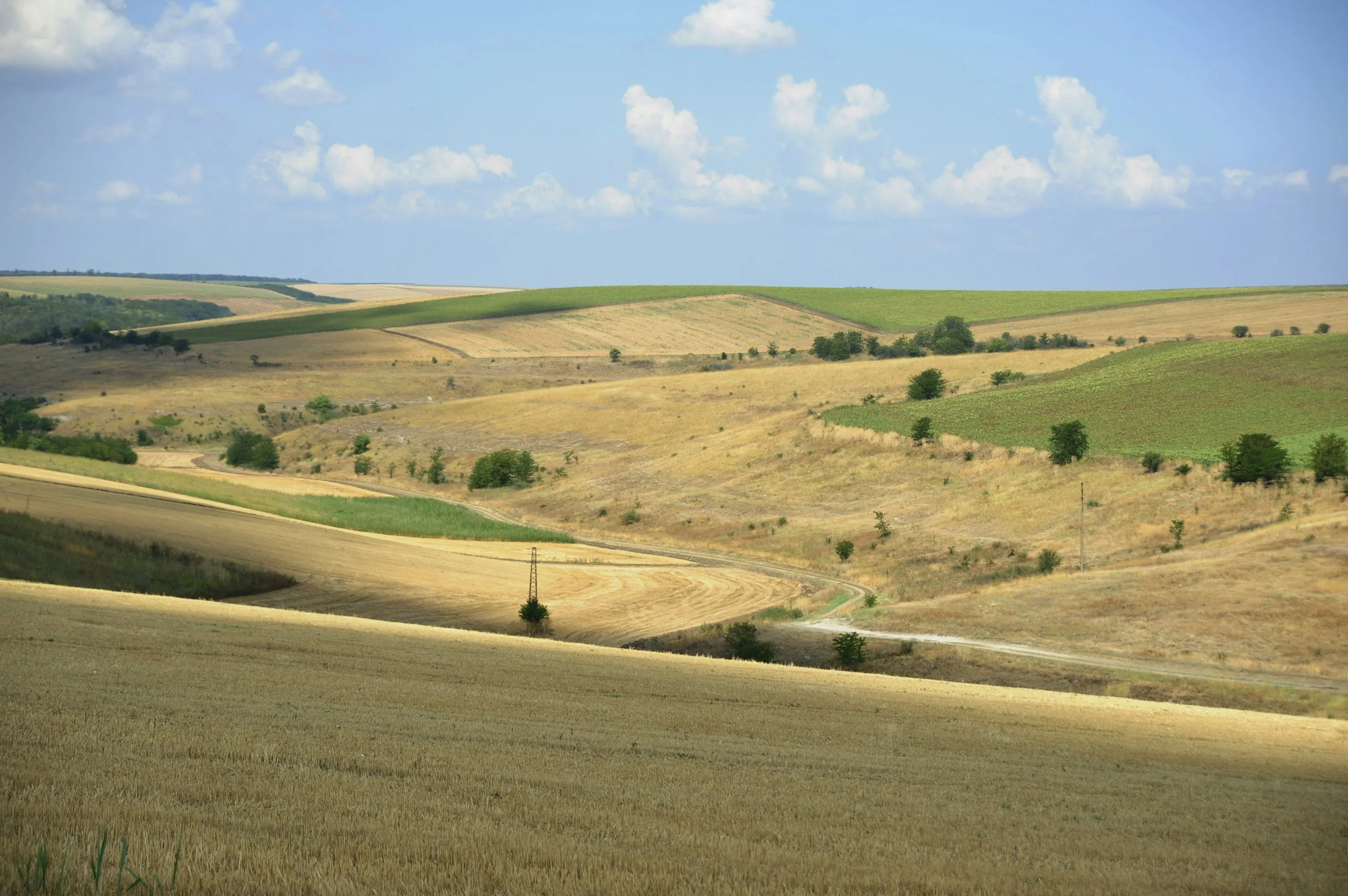 Rolling hills with patches of green and golden fields under a partly cloudy blue sky.