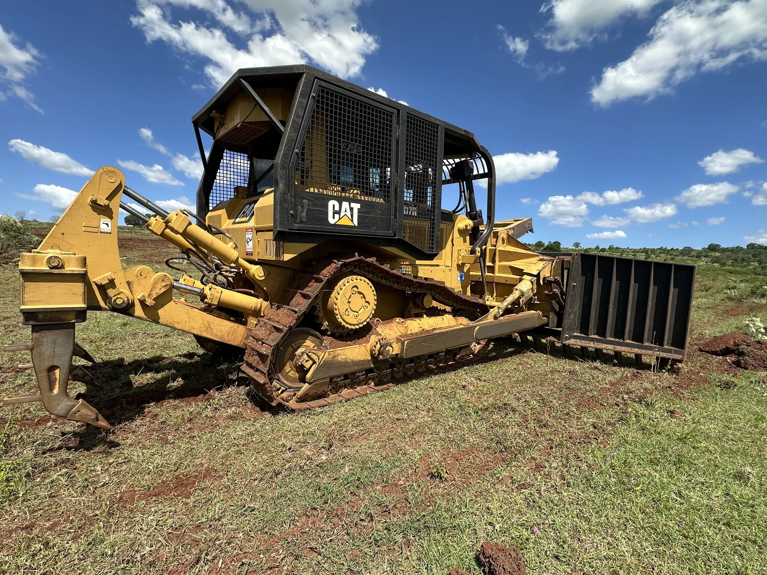 Yellow Caterpillar bulldozer with black metal cab on grassy terrain, blue sky with scattered clouds in background.