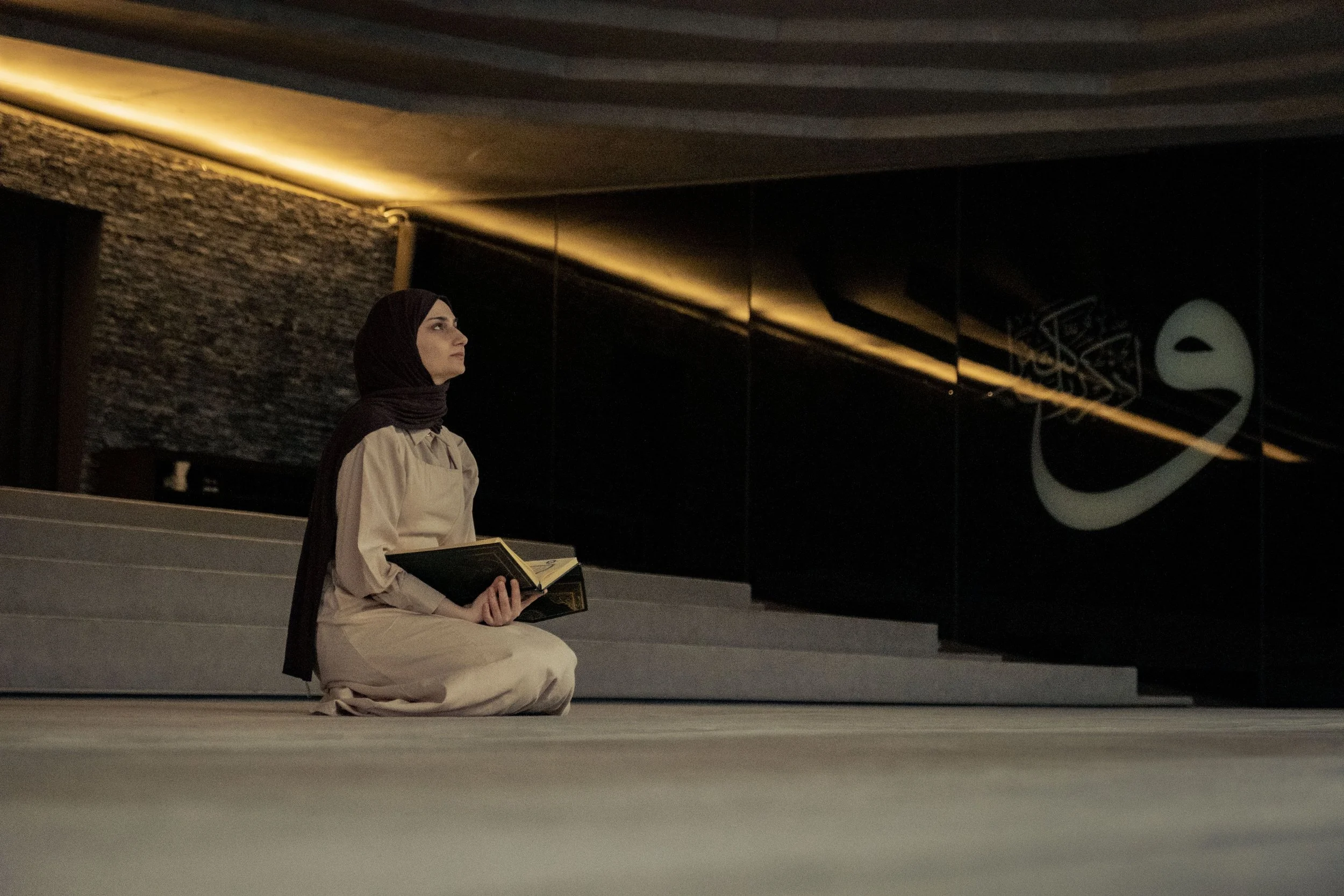 A woman sitting alone reading the Quran, looking reflective
