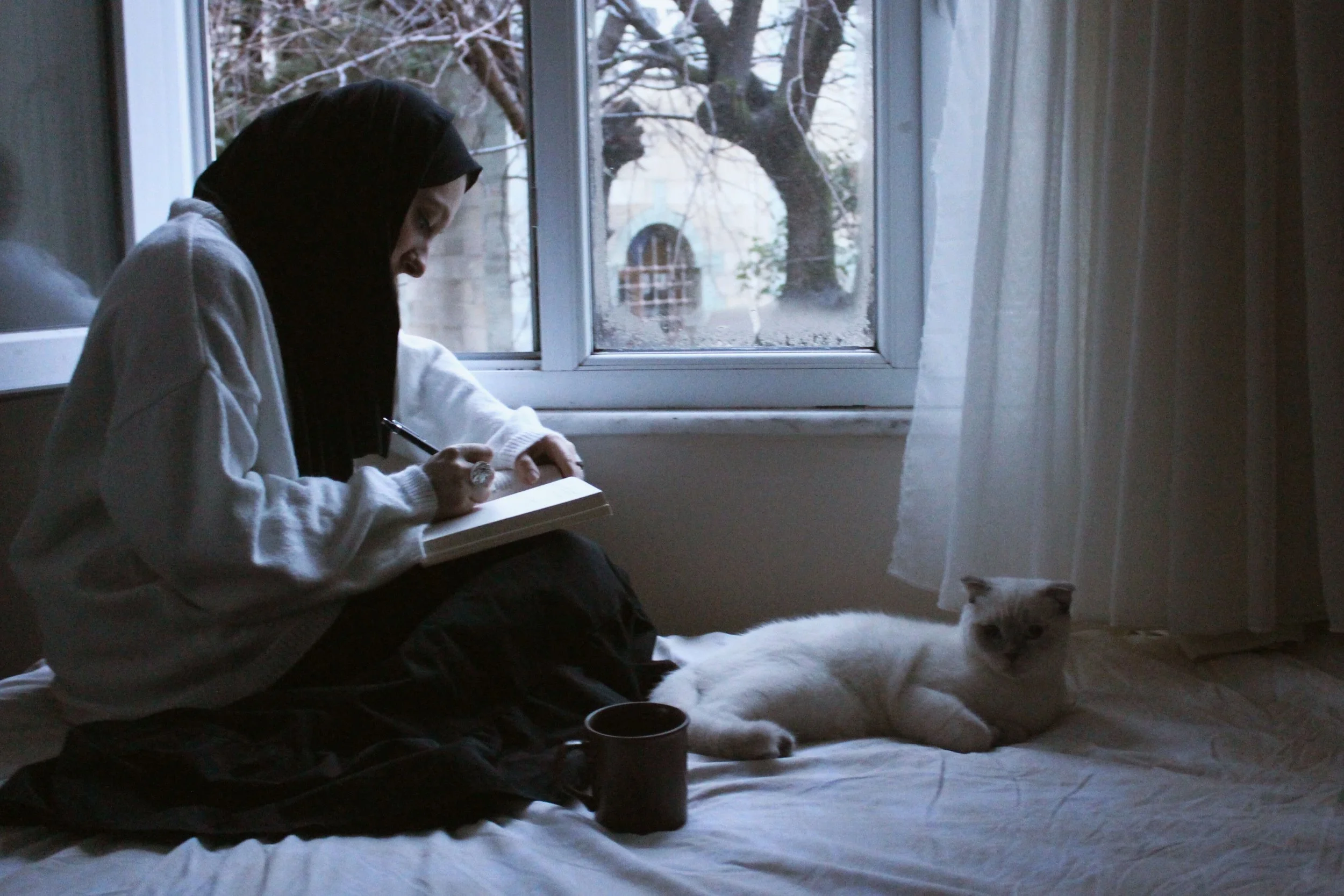 A muslim woman journaling at home with a cat on her side