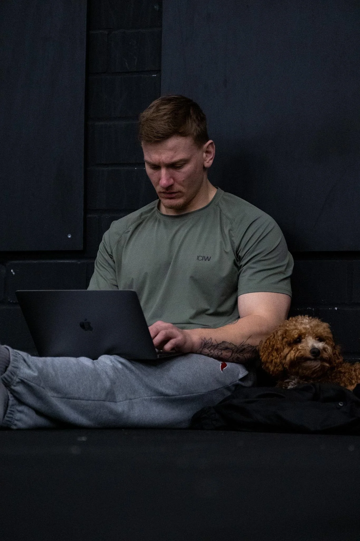 Ein online Fitnesstrainer sitzt auf dem Boden, blickt auf einen Laptop und schreibt Trainingspläne.