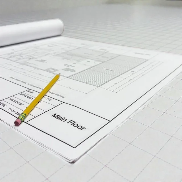 Architectural blueprints on grid paper with ayellow pencil placed on the plans.