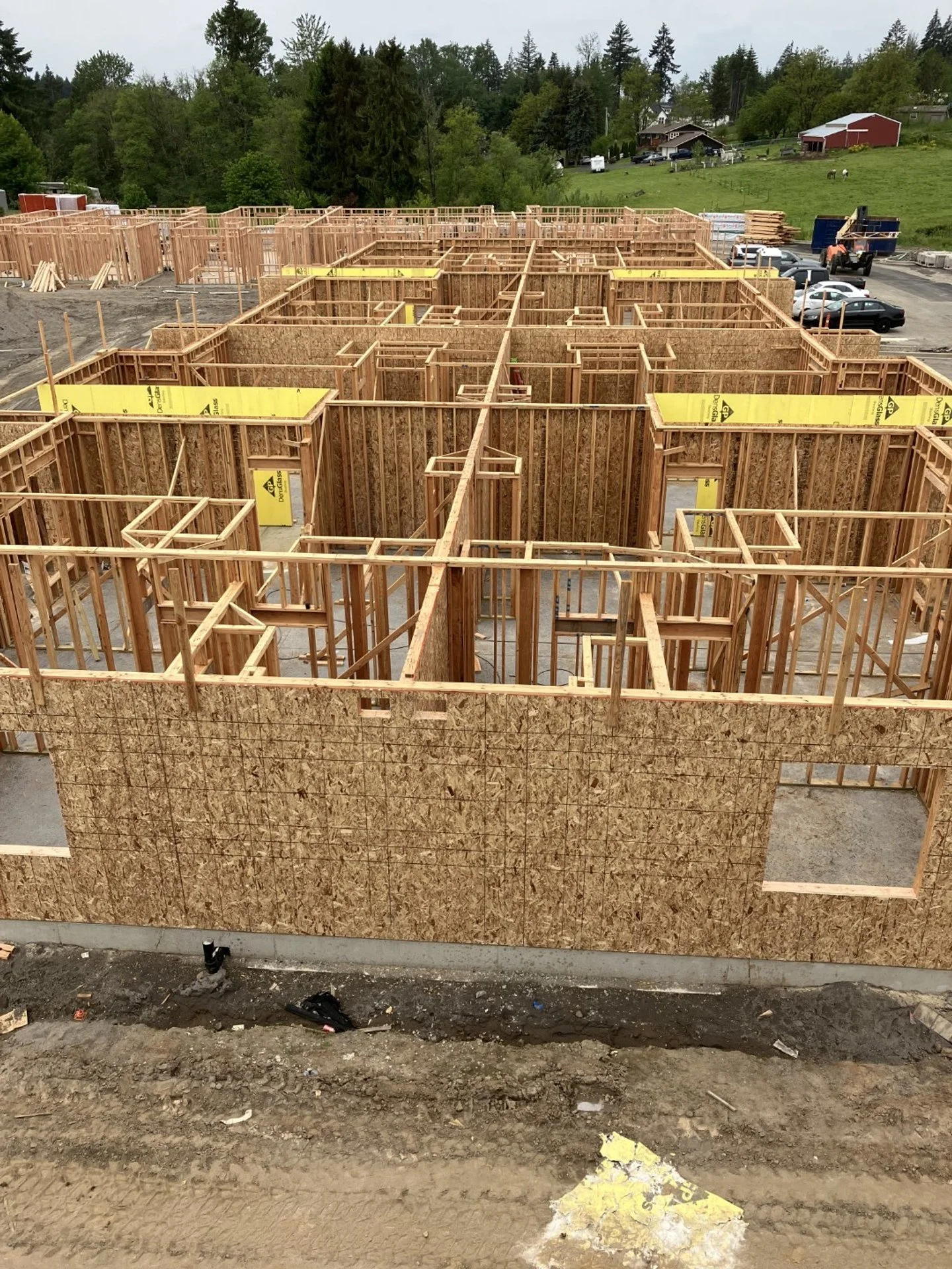 Wooden framing for the walls of a building under construction, with a view of a green landscape and parked cars in the background.