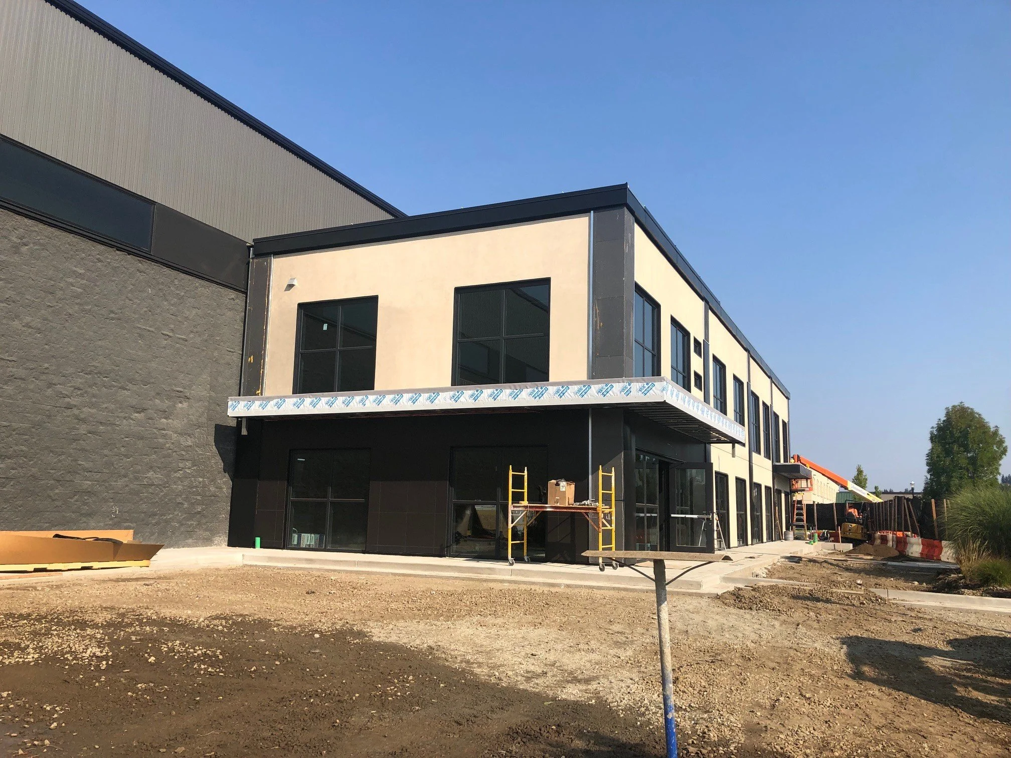 Construction site with a modern building under construction, featuring black and beige exterior walls, large windows, and construction equipment around.