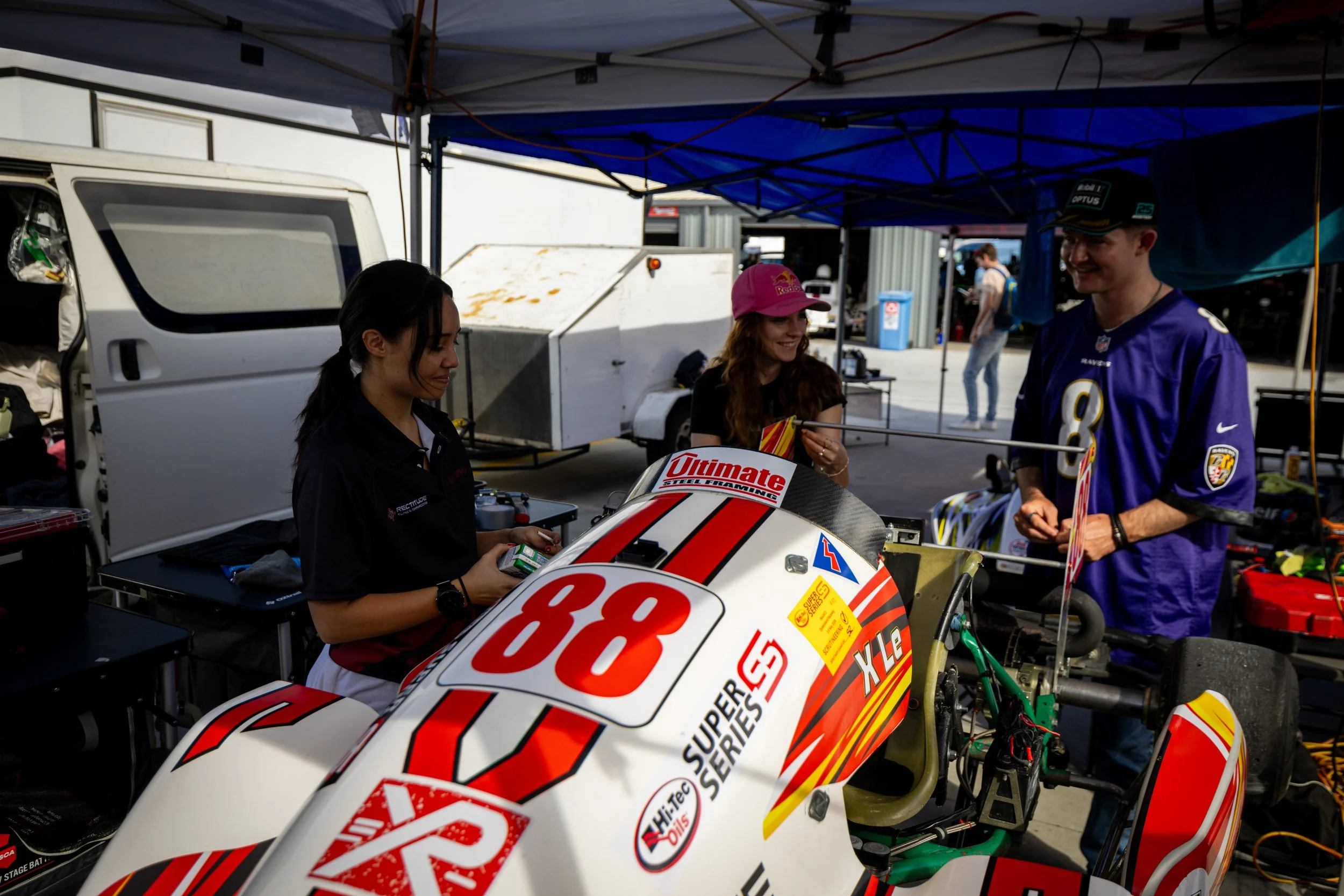 X Le and friends standing around the # 88 Superkart at a racing event, with a team tent and equipment in the background.
