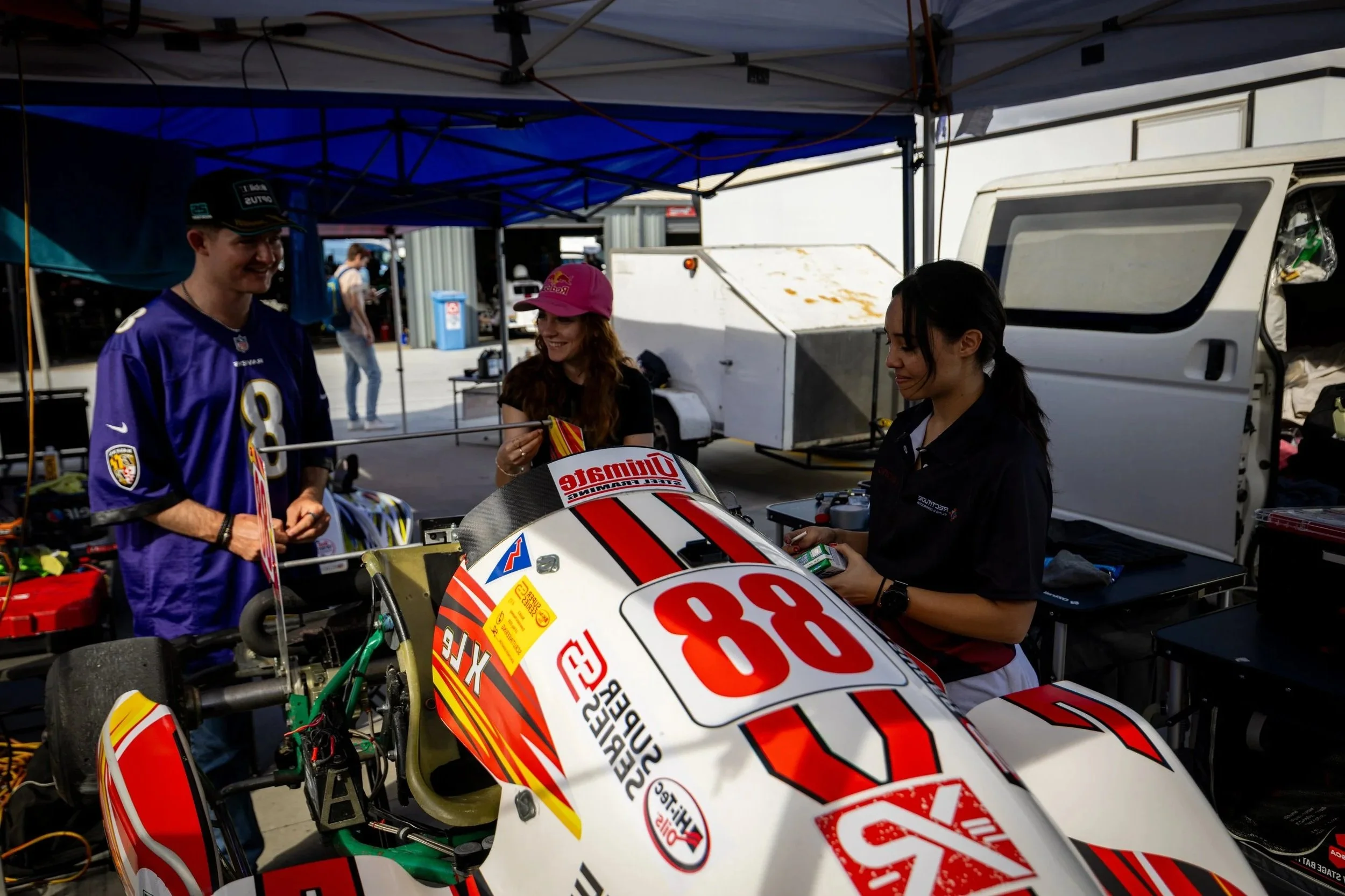 X Le and friends standing around the # 88 Superkart at a racing event, with a team tent and equipment in the background.